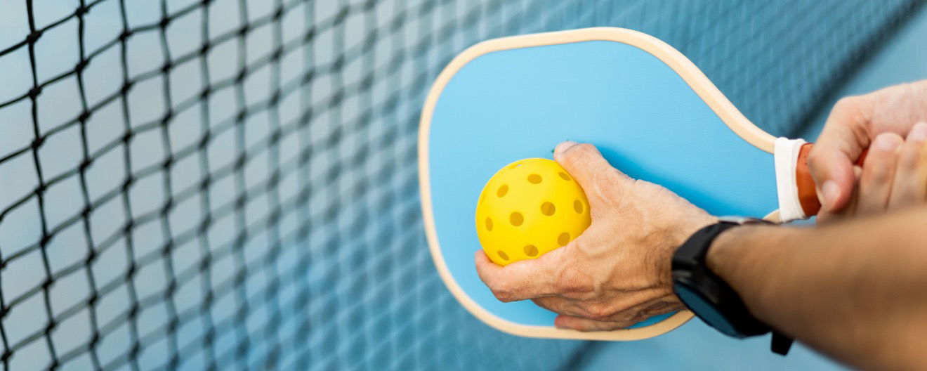 A man holding a pickleball paddle and ball.