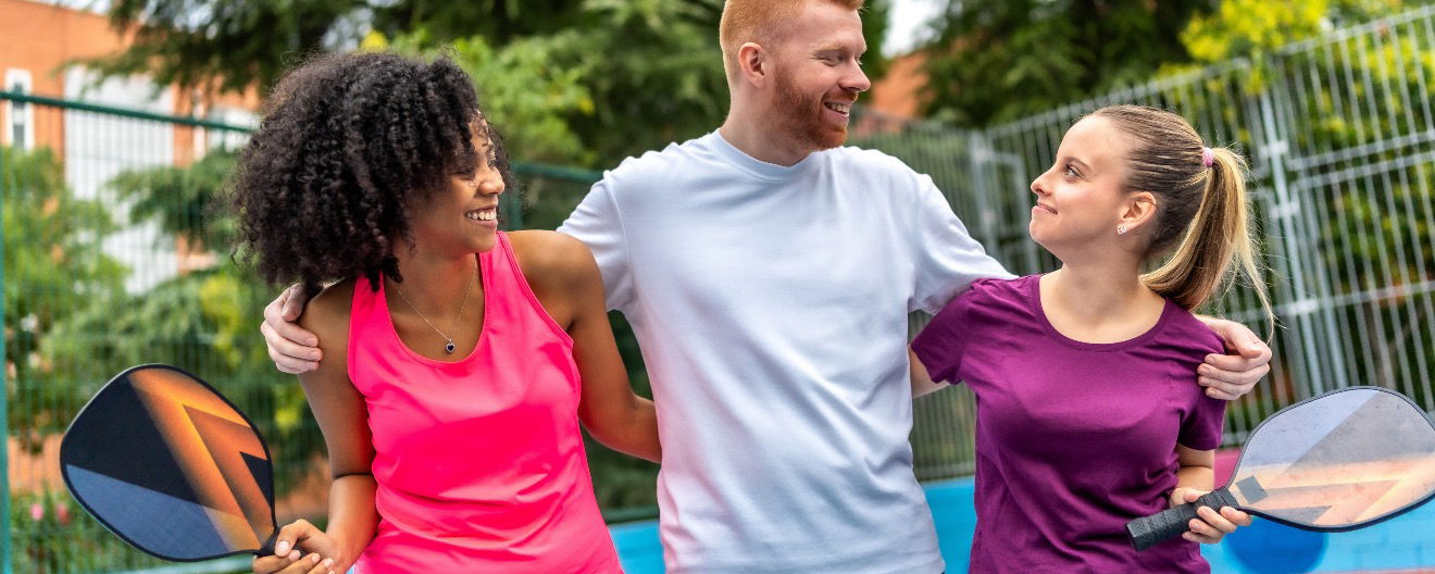 Three pickleball players smiling at each other.