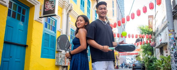 Jimmy Liong and Mia Athilla posing on a street with pickleball paddles.