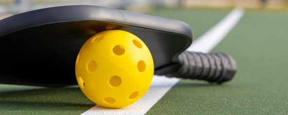 A pickleball and pickleball paddle on a pickleball court.