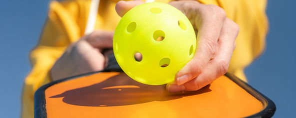 A person holding a paddle and pickleball.