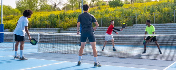 A group of young people playing pickleball outdoors.