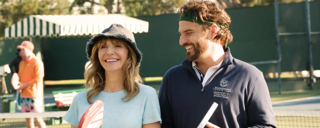 Mary Steenburgen and Jake Johnson smiling on a pickleball court.