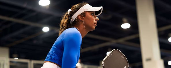 Tyra Black in a blue long sleeve shirt, white vizor, white skirt.
