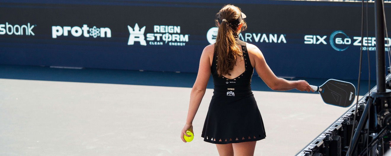 Back of Jorja Johnson while she's paddle tapping in a black dress with cutouts on the hem
