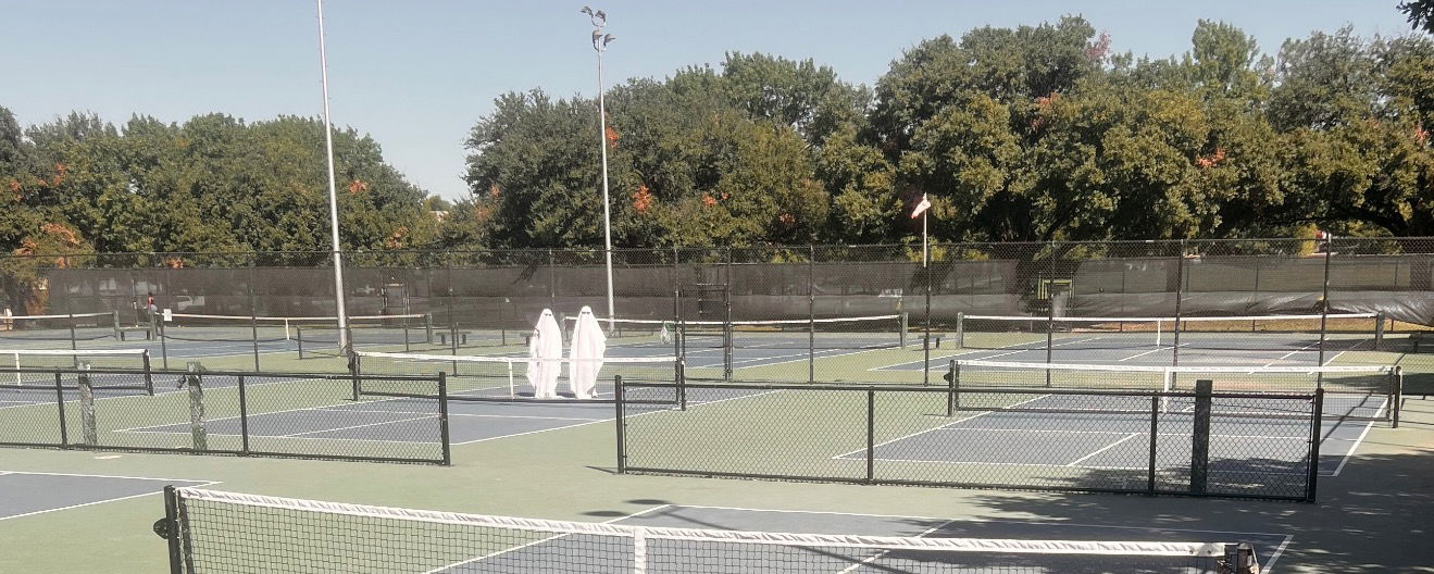 Two sheet ghosts on an empty pickleball court.