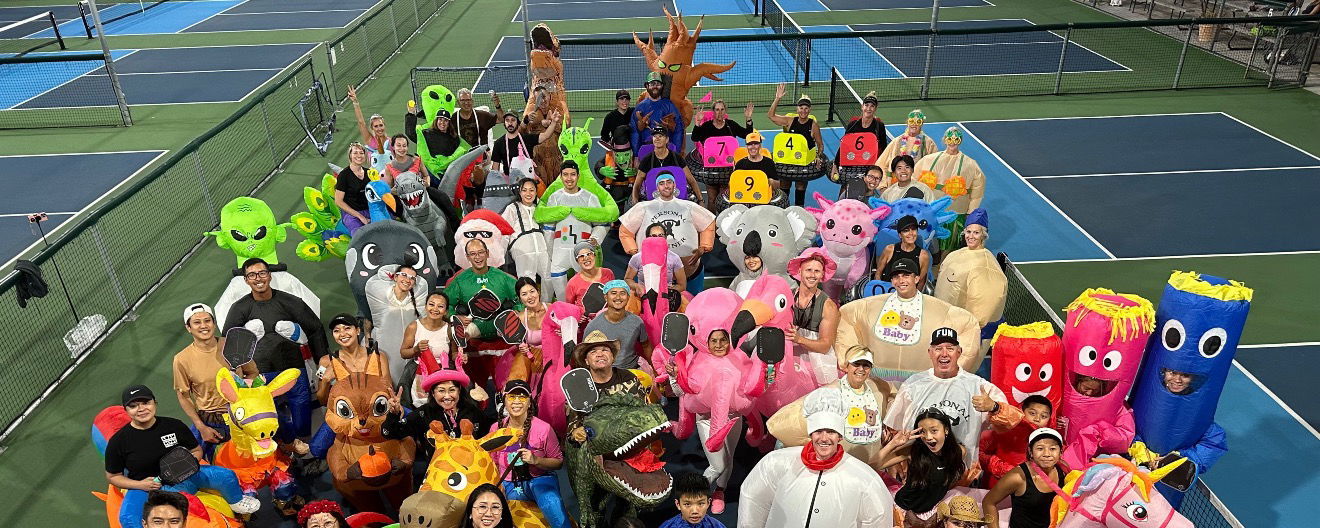 Group of people dressed in inflatable costumes playing pickleball.