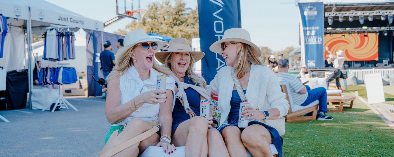 Three women in hats smiling and laughing on Pickleball Boulevard.