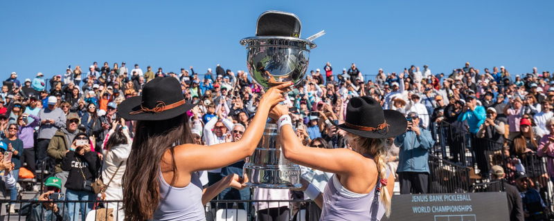 Anna Bright and Anna Leigh Waters wearing cowboy hats and holding up a trophy in front of a happy crowd.