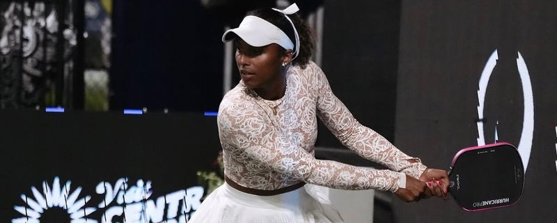 Black wearing a white lace top, white skirt, and white visor and hair bow.