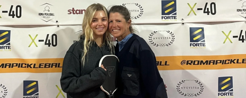 Anna Leigh Waters and Leigh Waters posing on a plaform at a pickleball facility in Italy.