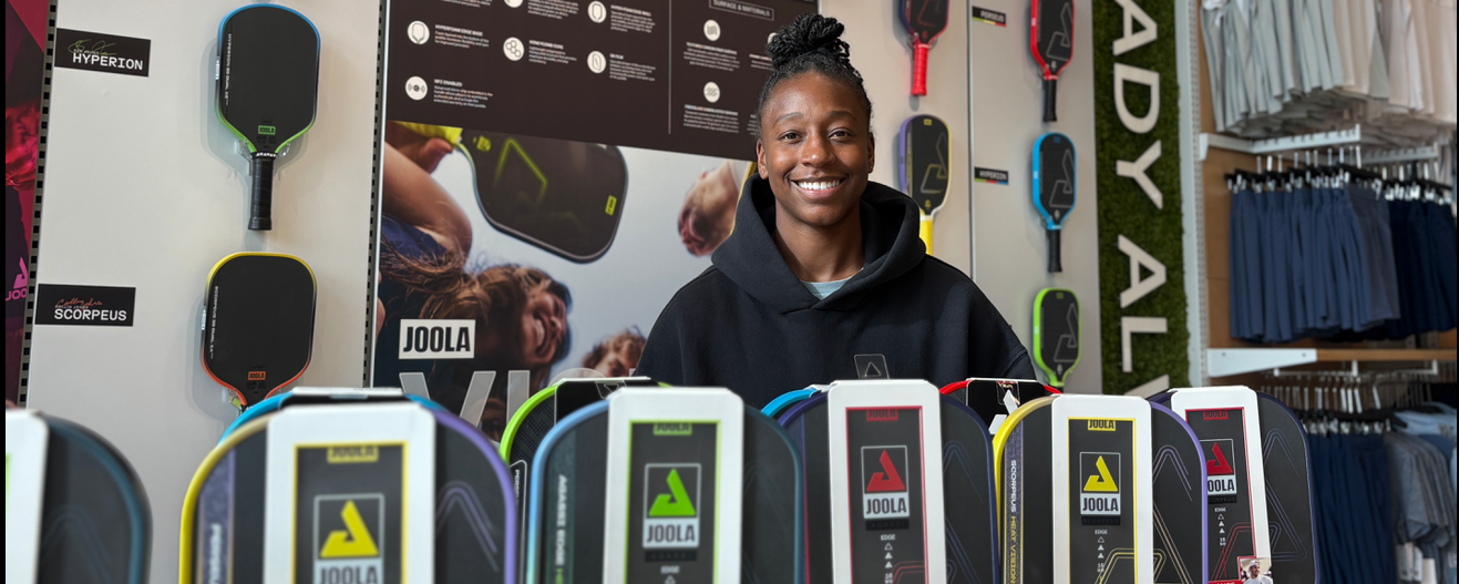 Jewell Loyd smiling, surrounded by pickleball paddles.