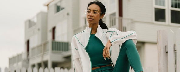 Model wearing a green sports bra and matching leggings with a white jacket over top.