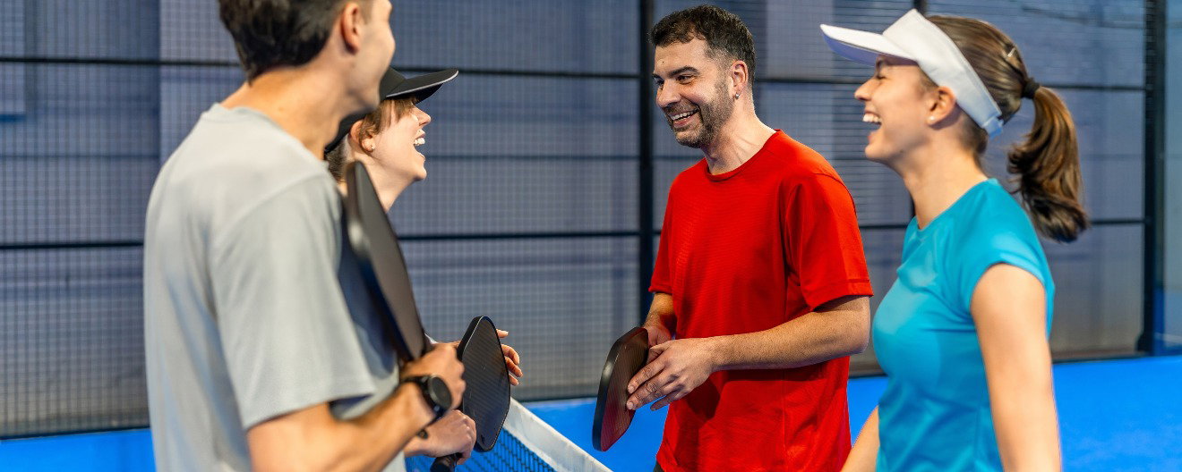 A group of four people laughing on the pickleball court.