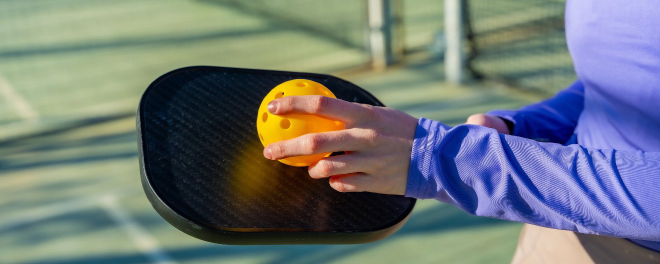 A player holding a pickleball paddle and a ball.