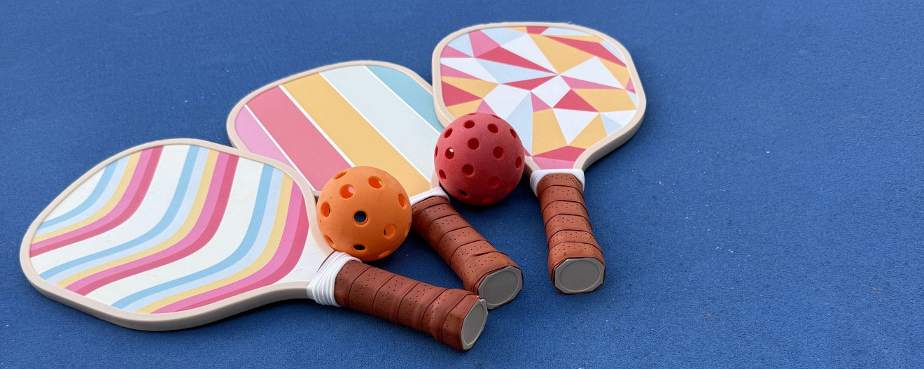 Three multi-colored pickleball paddles laying on a blue court.