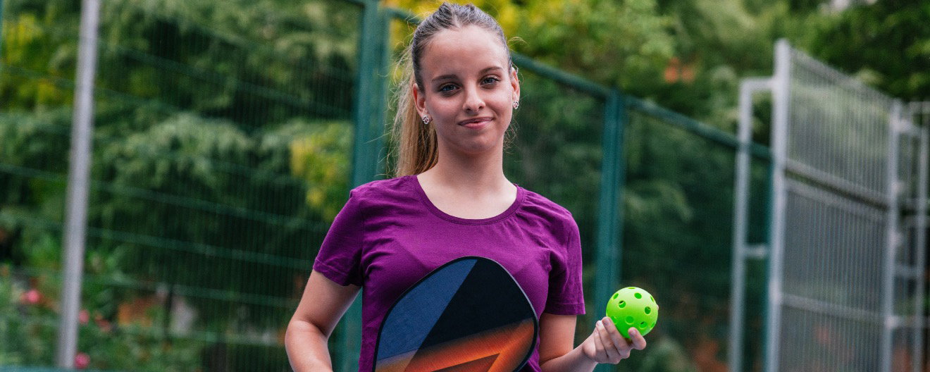A girl holding a pickleball paddle and pickleball.